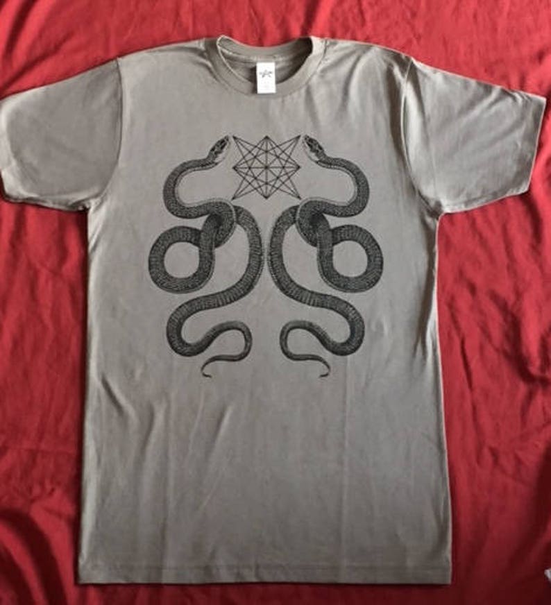 K&ouml;nnte beinhalten: Ein graues T-Shirt mit einem schwarz-wei&szlig;en Grafikdruck von zwei Schlangen, die sich gegen&uuml;berstehen, und einem geometrischen Stern in der Mitte.