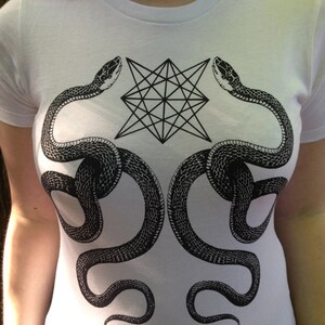 K&ouml;nnte beinhalten: Wei&szlig;es T-Shirt mit einem schwarz-wei&szlig;en grafischen Design aus zwei Schlangen, die sich um einen geometrischen Stern winden.