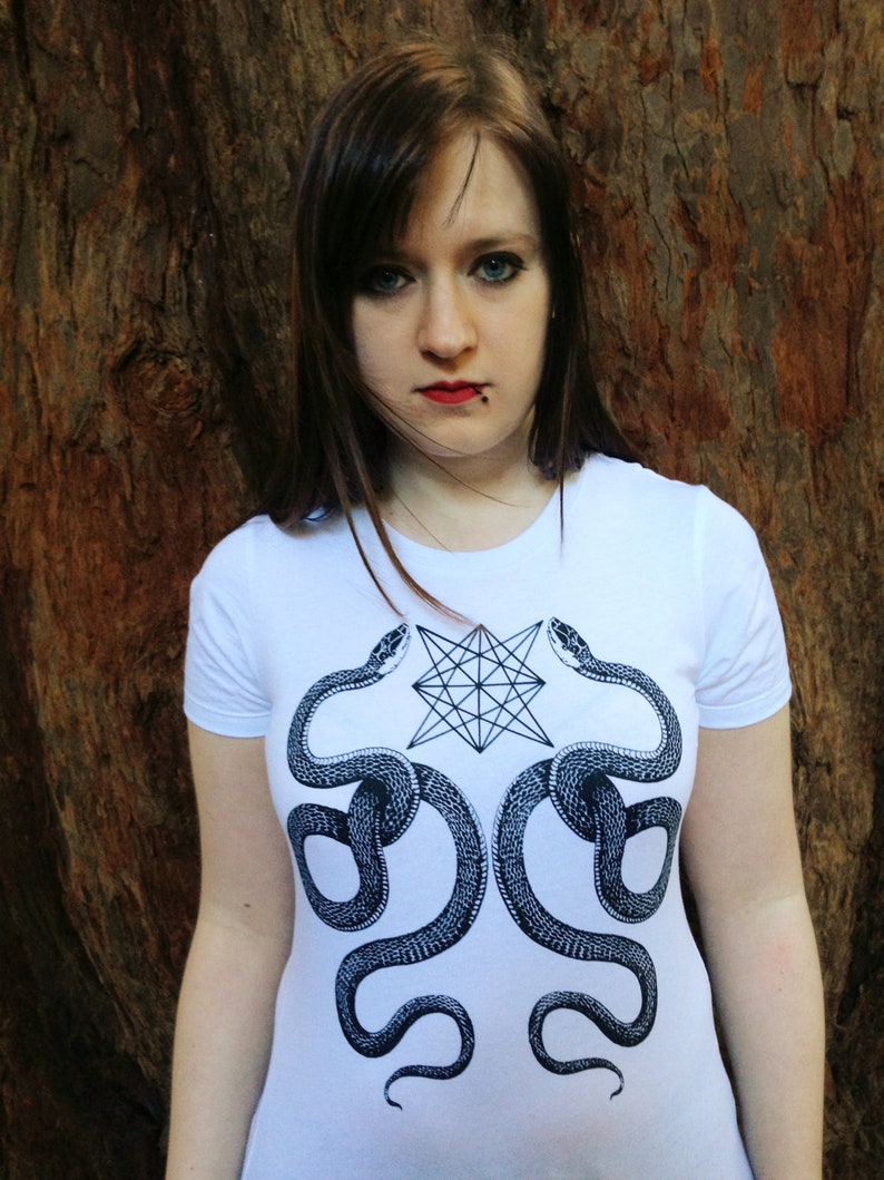 K&ouml;nnte beinhalten: Ein wei&szlig;es T-Shirt mit einem schwarz-wei&szlig;en Grafikdruck von zwei Schlangen, die sich um einen geometrischen Stern winden. Die Schlangen schauen sich an, die K&ouml;pfe oben am Design.