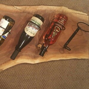 May include: Five wine bottles are displayed on a wooden wine rack. The bottles are held in place by metal rings. The rack is made of a natural wood with a rustic finish.