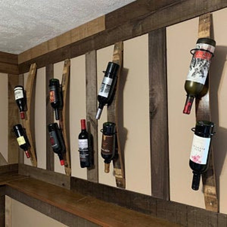 May include: A wall mounted wine rack made from reclaimed wood barrel staves with metal bottle holders. The rack is holding eight bottles of wine.