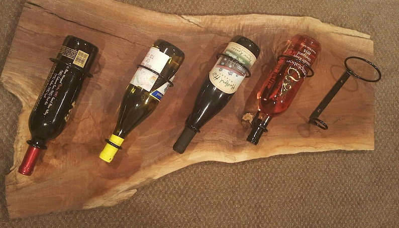 May include: Five wine bottles are displayed on a wooden wine rack. The bottles are held in place by metal rings. The rack is made of a natural wood with a rustic finish.