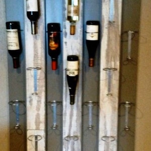 May include: A rustic wooden wine rack with a distressed white paint finish. The rack features metal rings to hold wine bottles and is mounted on a wall.