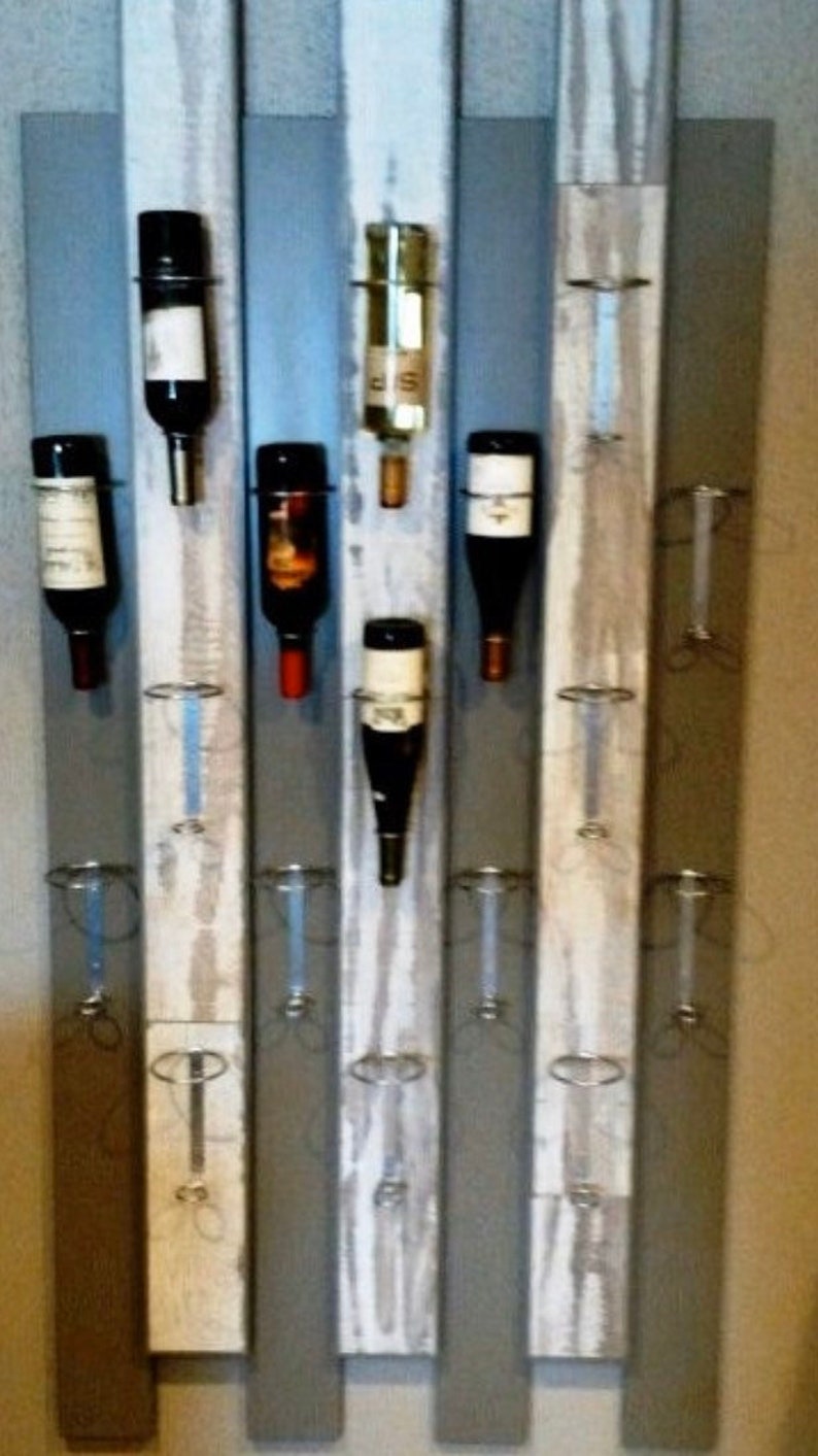 May include: A rustic wooden wine rack with a distressed white paint finish. The rack features metal rings to hold wine bottles and is mounted on a wall.