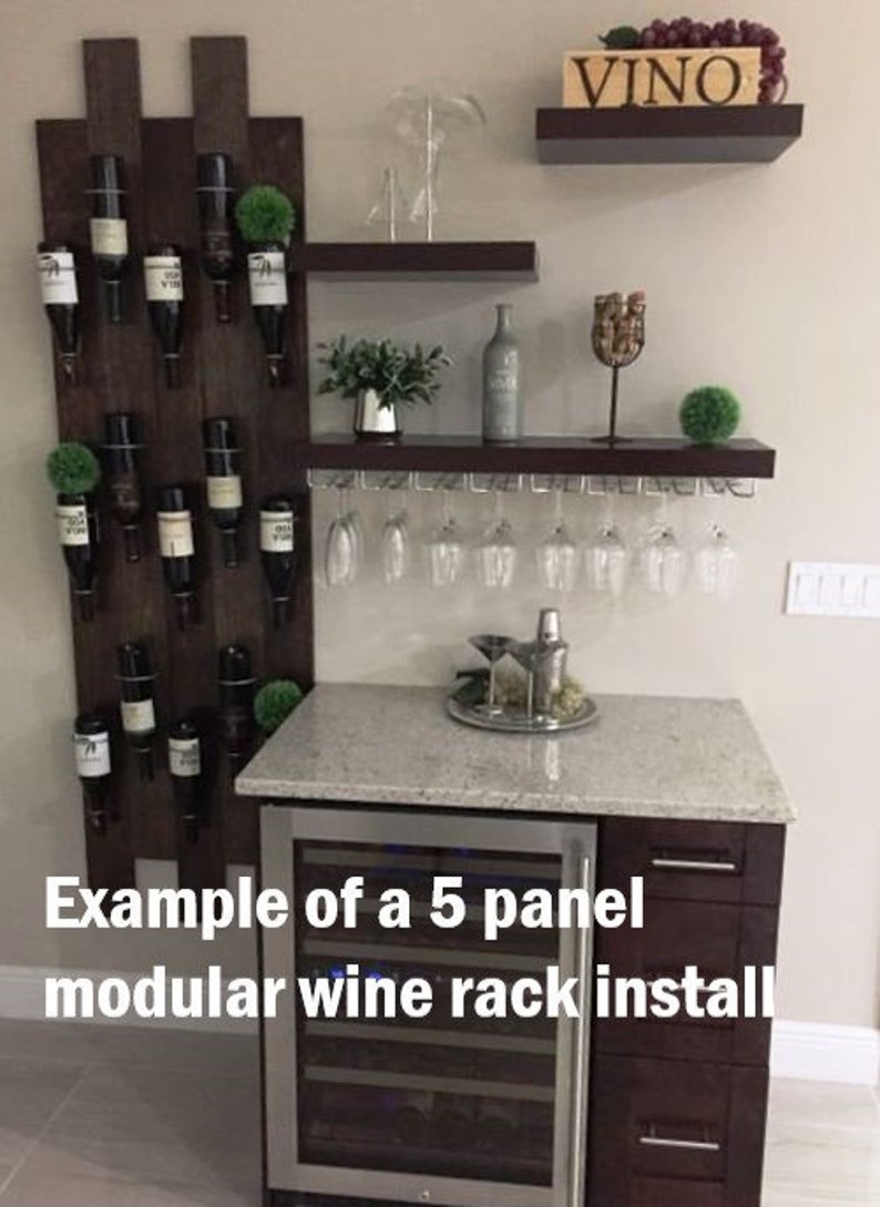 May include: A five-panel modular wine rack with a dark wood finish, holding wine bottles and glasses. The rack is mounted on a wall and includes a small wine cooler with a stainless steel door. The text "Example of a 5 panel modular wine rack install" is visible at the bottom of the image.