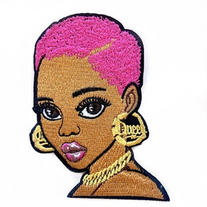 Może przedstawiać: Naszywka haftowana do prasowania przedstawiająca kreskówkową ilustrację kobiety z krótkimi różowymi włosami, brązową skórą i złotą biżuterią. Kobieta nosi złoty naszyjnik z łańcuszkiem i duże złote kolczyki koła.
