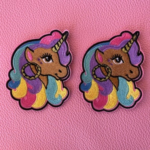 May include: Two colorful embroidered unicorn patches with rainbow manes and brown faces. Each patch has a gold hoop earring.