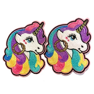 May include: Two colorful embroidered unicorn patches with gold hoop earrings. The unicorns have pink, purple, blue, yellow, and green manes and tails.