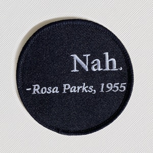 May include: A black circular patch with white embroidered text that reads "Nah. -Rosa Parks, 1955".