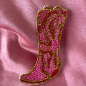 May include: Pink embroidered iron-on patch of a cowboy boot with gold stitching.