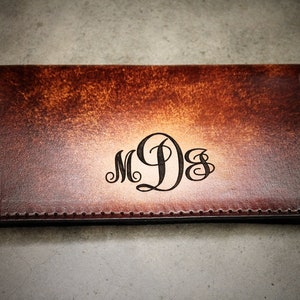 May include: A brown leather checkbook cover with a monogram of the initials "MDS" in a script font.