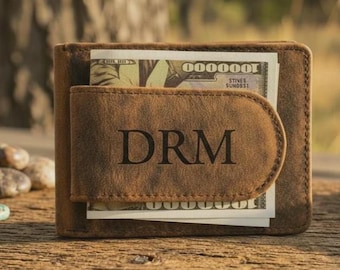 May include: A brown leather wallet with a money clip. The wallet is personalized with the initials "DRM" engraved on the front. The wallet is filled with U.S. currency.