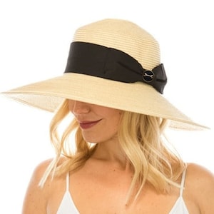 May include: A wide-brimmed straw hat with a black ribbon band and a decorative button. The hat has a natural beige color and is designed to provide sun protection. The brim is wide, offering ample shade. The hat is a stylish accessory for sunny days.