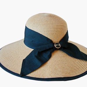 May include: A wide-brimmed straw hat with a black ribbon tied in a bow at the front. The hat has a black trim around the brim and a small metal button on the bow.