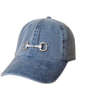 May include: A blue denim baseball cap with a silver equestrian-style bit detail on the front.