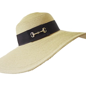 May include: A wide-brimmed straw sun hat with a black ribbon and a gold metal accent. The hat is beige and has a woven texture.