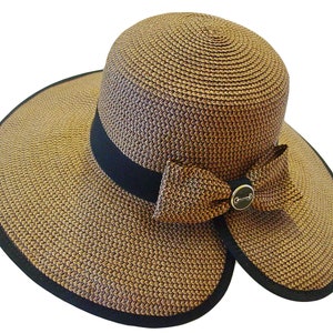 May include: A woven sun hat with a wide brim and a black ribbon. The hat features a decorative bow with a gold-colored metal accent. The hat's brim has a black trim.