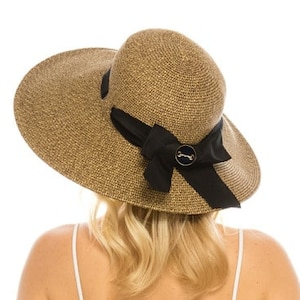 May include: A wide-brimmed sun hat with a woven straw design. The hat features a black ribbon tied in a bow and a decorative button. The hat is tan and is designed for sun protection.