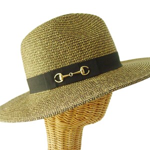 May include: A woven straw fedora hat with a black band and gold-colored metal horse bit detail. The hat has a wide brim and is displayed on a wicker head form. The hat's color is a mix of tan and dark brown.