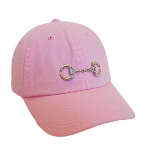 May include: A pink baseball cap with a silver and rhinestone horse bit design.