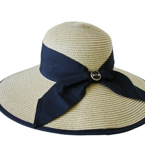 May include: A wide-brimmed straw hat with a black ribbon tied in a bow at the front. The hat has a black trim around the brim and a small silver button with a design on it.