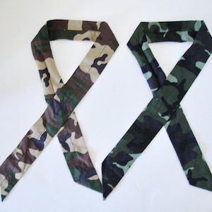 Op de afbeelding: Twee camouflage-gekleurde stoffen hoofdbanden, een in een groen, zwart en bruin patroon en de andere in een tan, groen en bruin patroon.