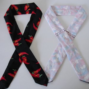 Op de afbeelding: Twee stoffen hoofdbanden, een zwarte met een rode chili peper print en een roze met een witte en blauwe abstracte print.