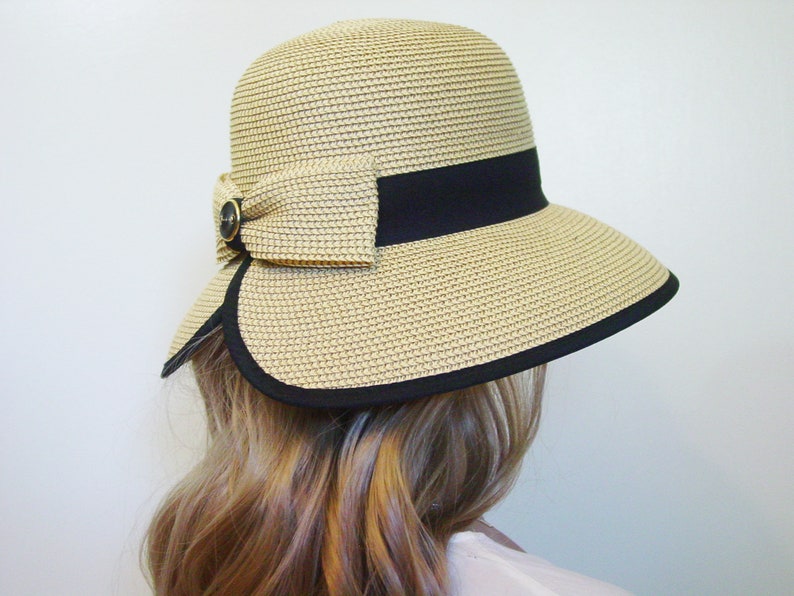 K&ouml;nnte beinhalten: Ein Strohhut mit schwarzem Band und Schleife. Der Hut hat eine breite Krempe und ist beige.
