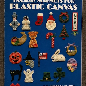 May include: A blue Leisure Arts craft leaflet titled Holiday Magnets for Plastic Canvas, featuring 23 designs by Nancy Dorman. The cover displays various plastic canvas needlepoint magnets including a Santa, pumpkin, flag, ghost, and heart shapes.