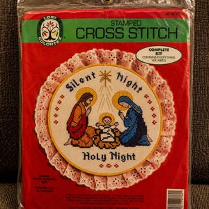 Op de afbeelding: Een Colortex gestempelde kruissteekset in een doorzichtige plastic zak. De verpakking bevat een rond borduurontwerp van een kerststal met de tekst Silent Night Holy Night. De afgewerkte maat is 25,4 cm, vermeld op de rode verpakking.