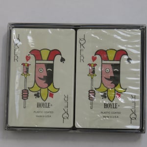 May include: Two decks of Hoyle plastic-coated playing cards in a clear plastic case. Each card features a joker with a red, yellow, and black jester hat and a smiling face. The text "HOYLE" and "Made in U.S.A." are visible.