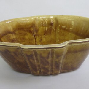 May include: A vintage, oval-shaped ceramic planter in shades of brown and yellow. The planter has a glossy finish and a ribbed design on the sides. The interior is a darker brown, contrasting with the lighter exterior.