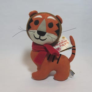 May include: A plush orange tiger with black stripes, wearing a red scarf. The tiger has a brown and orange head with a gray nose and black whiskers. A tag reads "Dream Pet?" This stuffed animal is a cute and cuddly toy.