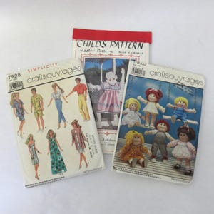 May include: Three vintage sewing pattern booklets. One booklet features illustrations of dolls, another shows a child in a pink dress, and the third displays fashion illustrations. The booklets are labeled "Simplicity" and "Crafts/Ouvrages".