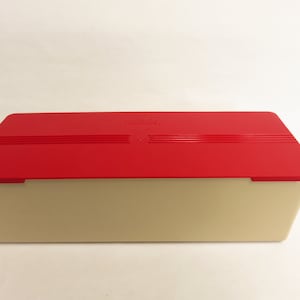 May include: A rectangular storage container with a red lid and a beige base. The lid has three horizontal lines and the word "Tupperware" is visible. The container is designed for food storage.