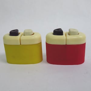 May include: Two vintage salt and pepper shakers. One is yellow, the other is red. Both have a cream-colored top with a black and cream-colored button. The sides of the shakers have a ribbed texture.