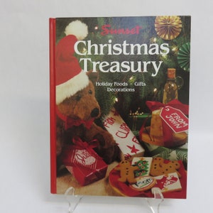 May include: A hardcover book titled Sunset Christmas Treasury: Holiday Foods, Gifts, Decorations. The cover features a brown teddy bear wearing a Santa hat, wrapped gifts with tags labeled From Claire and From John, and gingerbread cookies on a plate.