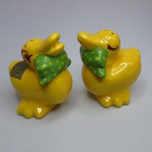 May include: A pair of yellow ceramic duck salt and pepper shakers. Each duck has a green scarf with yellow polka dots and a smiling face. One shaker has a sticker that reads "California Mics".