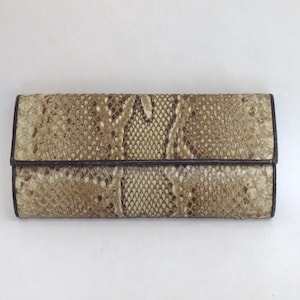 May include: A rectangular clutch wallet with a snakeskin pattern in shades of beige, brown, and tan. The wallet has a dark brown border and a flap closure. The snakeskin texture is visible across the surface.