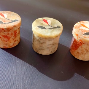 May include: Three small, round, decorative boxes made of marble with floral designs. The boxes are in shades of red, white, and green.