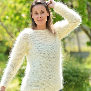 May include: A white fuzzy knit sweater with a round neckline and long sleeves. The sweater is made of a soft, lightweight yarn and has a relaxed fit.