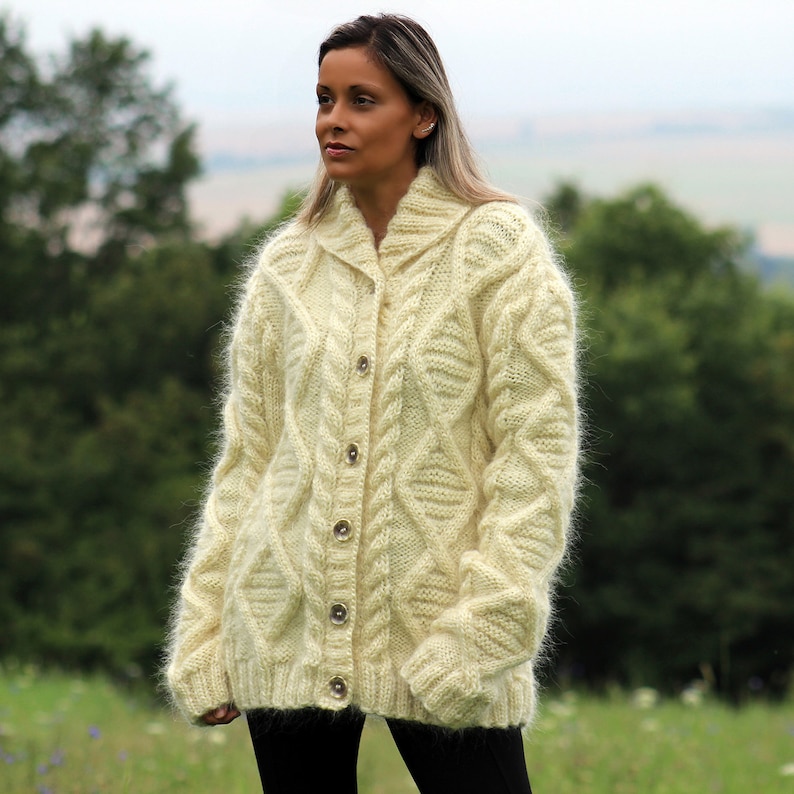 May include: A cream-colored, fuzzy, cable knit cardigan with a button closure. The cardigan has a relaxed fit and a collar.