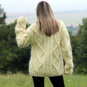 May include: A cream-colored fuzzy cable knit sweater with a loose fit and long sleeves.