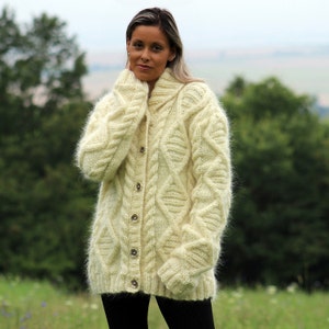 May include: A cream-colored fuzzy cardigan with a cable knit pattern and button closure.