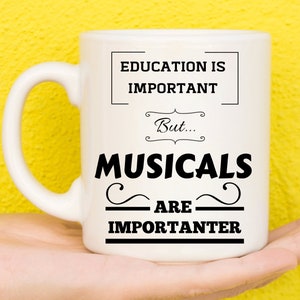 May include: White ceramic mug with a black inscription that reads "Education is important, but musicals are importanter".