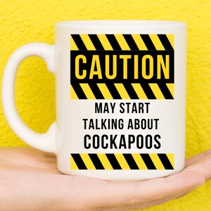 Könnte beinhalten: Weiße Keramiktasse mit einem schwarzen und gelben Warnschild-Design. Der Text auf der Tasse lautet "Vorsicht Kann anfangen, über Cockapoos zu sprechen".