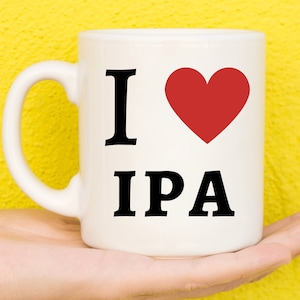 Può includere: Una tazza in ceramica bianca con un cuore rosso e la scritta "I love IPA" stampata su di essa.