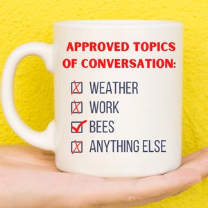 May include: White ceramic mug with a blue and red design. The mug says "APPROVED TOPICS OF CONVERSATION:" with a checkmark next to "BEES" and an X next to "WEATHER", "WORK", and "ANYTHING ELSE".