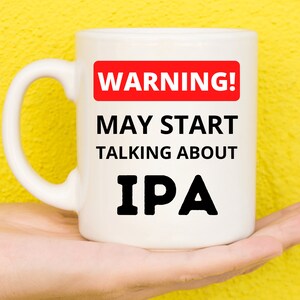 Può includere: Tazza in ceramica bianca con un cartello di avvertimento rosso che dice "ATTENZIONE! POTREBBE INIZIARE A PARLARE DI IPA".