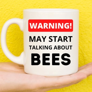 May include: White ceramic mug with a red warning sign that says "WARNING! MAY START TALKING ABOUT BEES".